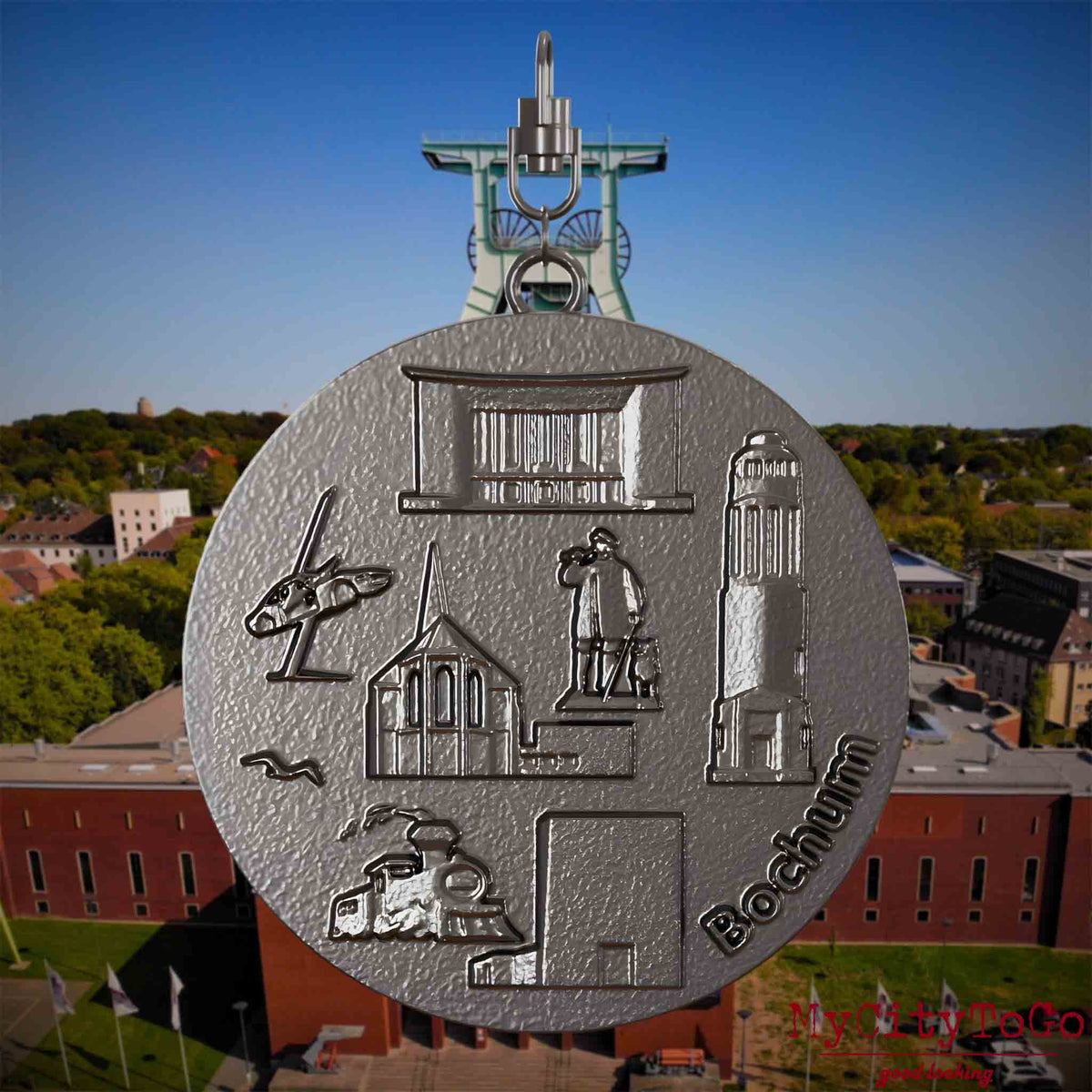 Halskette mit Drehwirbel und Rückseite eines Schmuckanhängers aus Titan, auf dem Reliefs bekannter Sehenswürdigkeiten der Stadt Bochum abgebildet sind. Den Hintergrund bildet eine Ansicht der Stadt Bochum .
