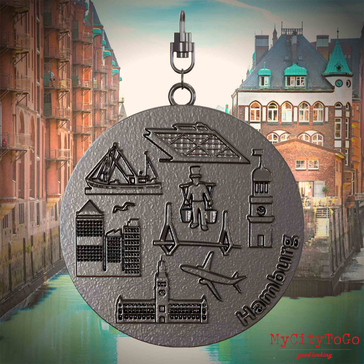 Halskette mit Drehwirbel und Vorderseite eines Schmuckanhängers aus Titan, auf dem Reliefs bekannter Sehenswürdigkeiten der Stadt Hamburg abgebildet sind. Den Hintergrund bildet eine Ansicht der Stadt Hamburg.