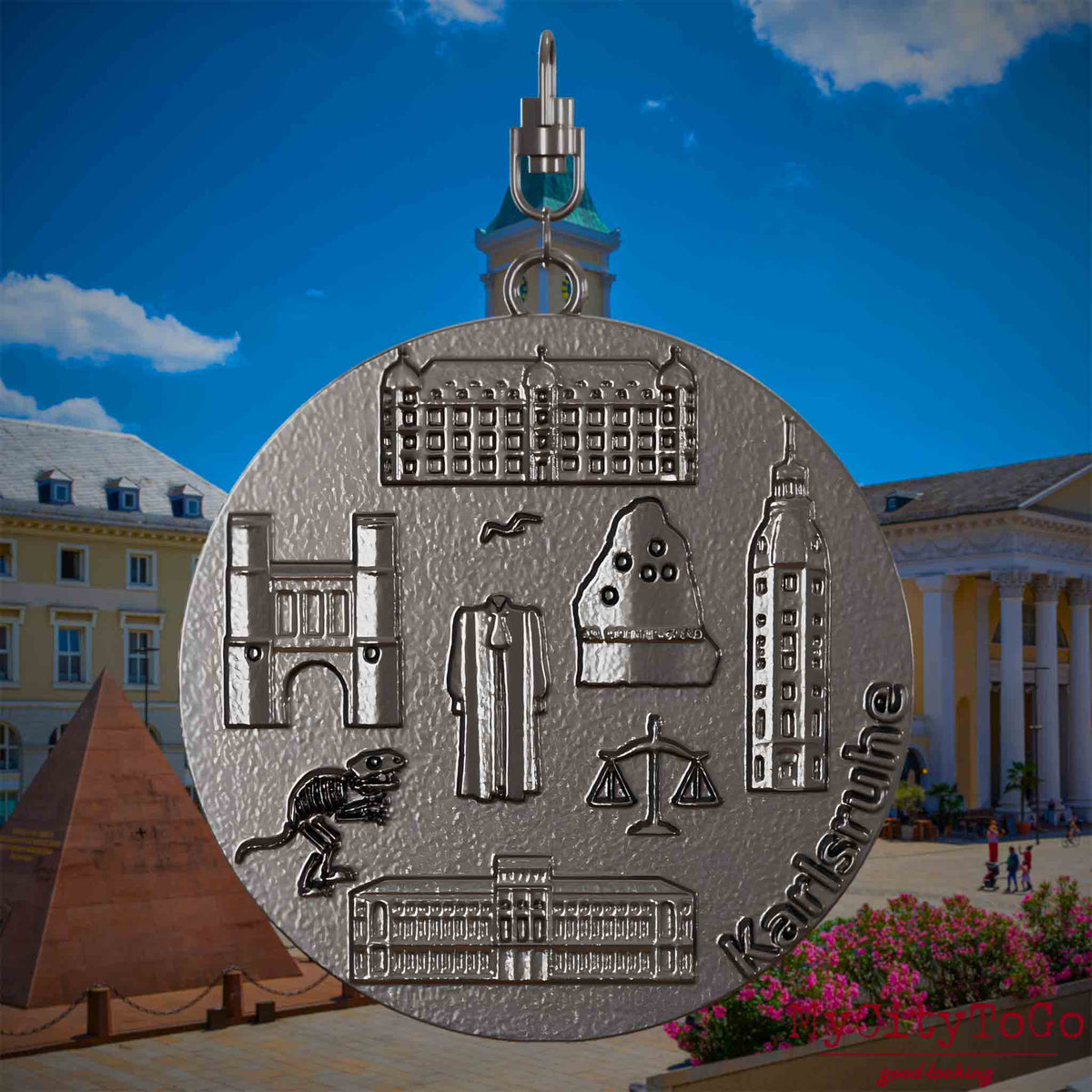 Halskette mit Drehwirbel und Rückseite eines Schmuckanhängers aus Titan, auf dem Reliefs bekannter Sehenswürdigkeiten der Stadt Karlsruhe abgebildet sind. Den Hintergrund bildet eine Ansicht der Stadt Karlsruhe .
