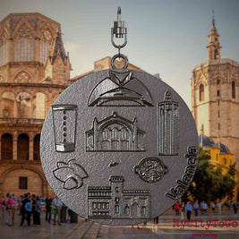 Halskette mit Drehwirbel und Vorderseite eines Schmuckanhängers aus Titan, auf dem Reliefs bekannter Sehenswürdigkeiten der Stadt Valencia abgebildet sind. Den Hintergrund bildet eine Ansicht der Stadt Valencia.
