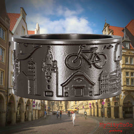 Ring aus Titan mit Reliefs bekannter Sehenswürdigkeiten der Stadt Muenster. Den Hintergrund bildet eine Ansicht der Stadt Muenster.