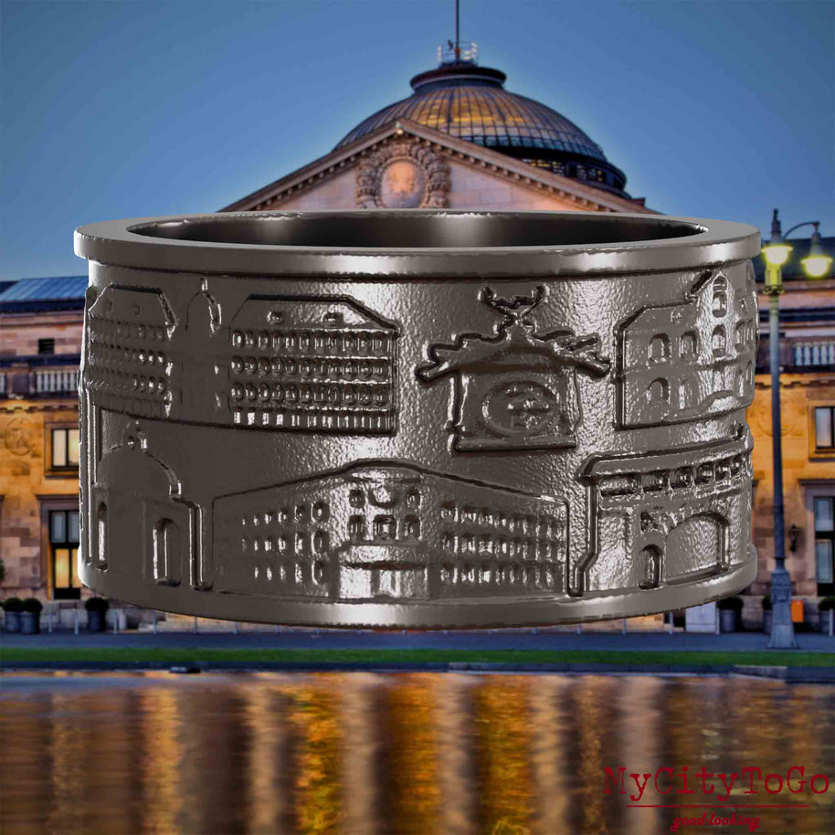 Ring aus Titan mit Reliefs bekannter Sehenswürdigkeiten der Stadt Wiesbaden. Den Hintergrund bildet eine Ansicht der Stadt Wiesbaden.