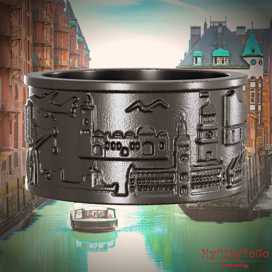 Ring aus Titan mit Reliefs bekannter Sehenswürdigkeiten der Stadt Hamburg. Den Hintergrund bildet eine Ansicht der Stadt Hamburg.