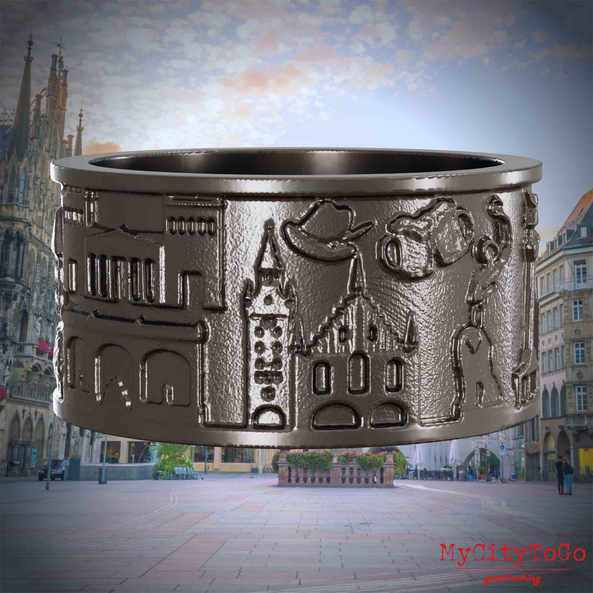 Ring aus Titan mit Reliefs bekannter Sehenswürdigkeiten der Stadt Muenchen. Den Hintergrund bildet eine Ansicht der Stadt Muenchen.