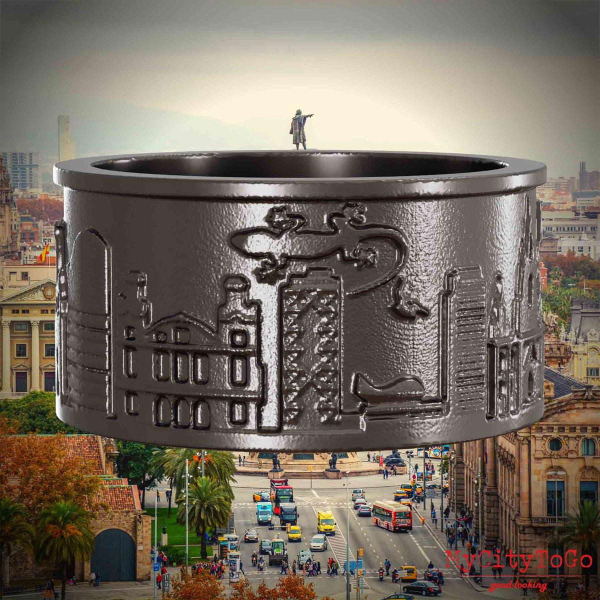 Ring aus Titan mit Reliefs bekannter Sehenswürdigkeiten der Stadt Barcelona. Den Hintergrund bildet eine Ansicht der Stadt Barcelona.