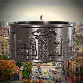 Ring aus Titan mit Reliefs bekannter Sehenswürdigkeiten der Stadt Barcelona. Den Hintergrund bildet eine Ansicht der Stadt Barcelona.