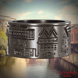 Ring aus Titan mit Reliefs bekannter Sehenswürdigkeiten der Stadt Leipzig. Den Hintergrund bildet eine Ansicht der Stadt Leipzig.