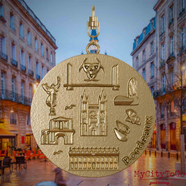 Halskette mit Drehwirbel und Vorderseite eines Schmuckanhängers aus vergoldetem Edelstahl, auf dem Reliefs bekannter Sehenswürdigkeiten der Stadt Bordeaux abgebildet sind. Den Hintergrund bildet eine Ansicht der Stadt Bordeaux.
