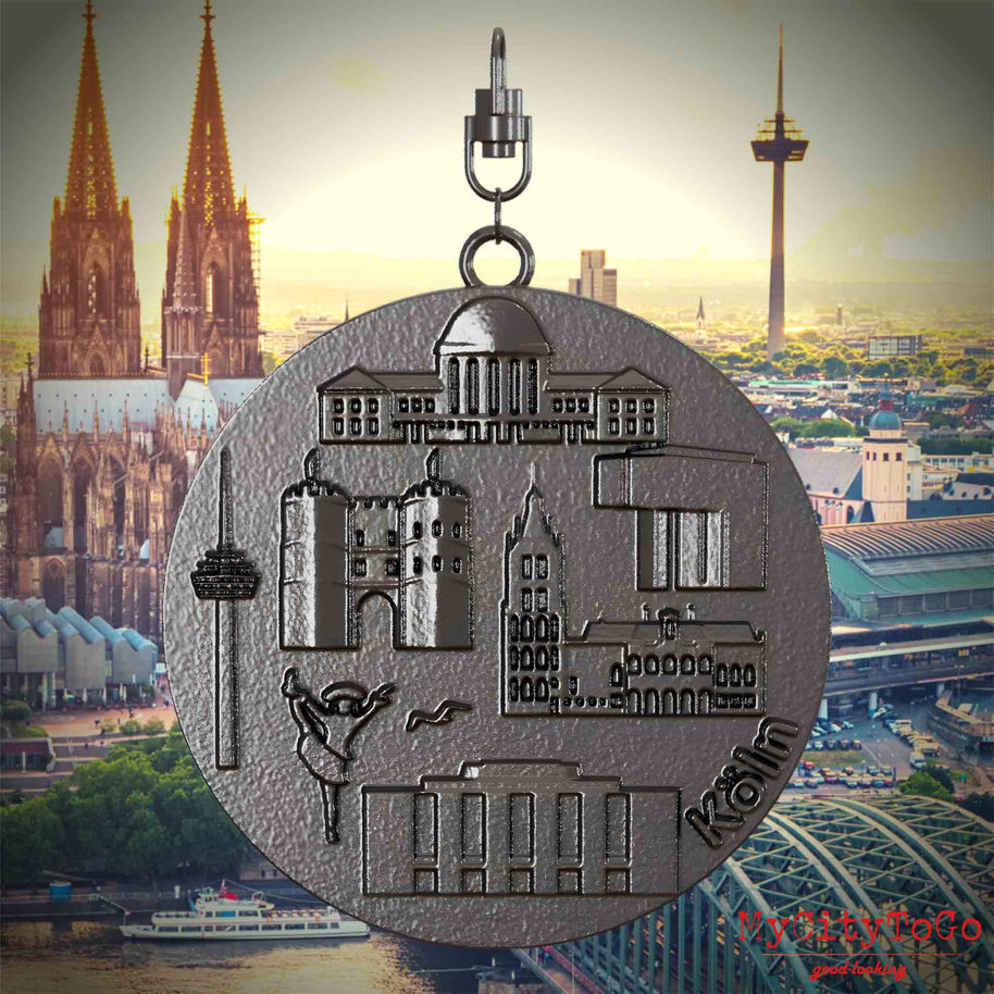 Halskette mit Drehwirbel und Rückseite eines Schmuckanhängers aus Titan, auf dem Reliefs bekannter Sehenswürdigkeiten der Stadt Koeln abgebildet sind. Den Hintergrund bildet eine Ansicht der Stadt Koeln.