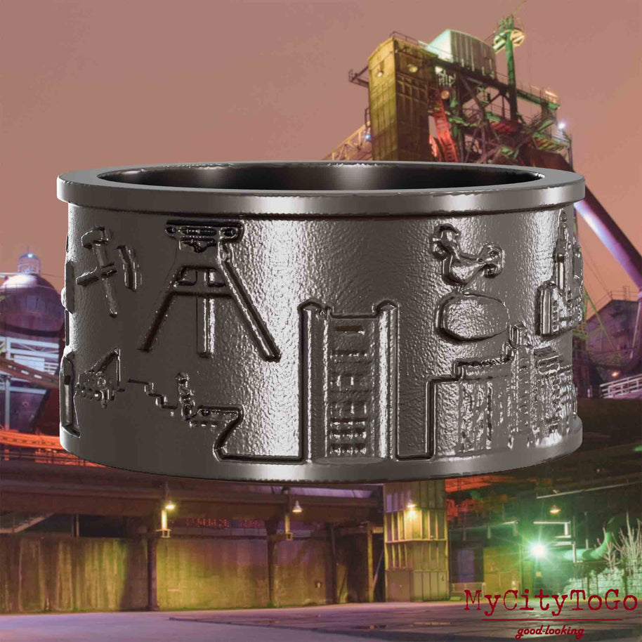 Ring aus Titan mit Reliefs bekannter Sehenswürdigkeiten der Stadt Duisburg. Den Hintergrund bildet eine Ansicht der Stadt Duisburg.