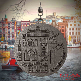 Halskette mit Drehwirbel und Rückseite eines Schmuckanhängers aus Titan, auf dem Reliefs bekannter Sehenswürdigkeiten der Stadt Amsterdam abgebildet sind. Den Hintergrund bildet eine Ansicht der Stadt Amsterdam.
