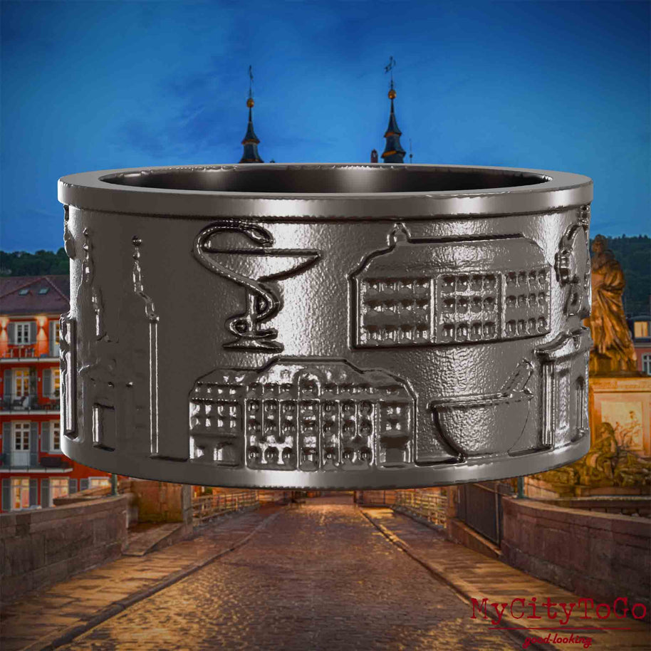 Ring aus Titan mit Reliefs bekannter Sehenswürdigkeiten der Stadt Heidelberg. Den Hintergrund bildet eine Ansicht der Stadt Heidelberg.