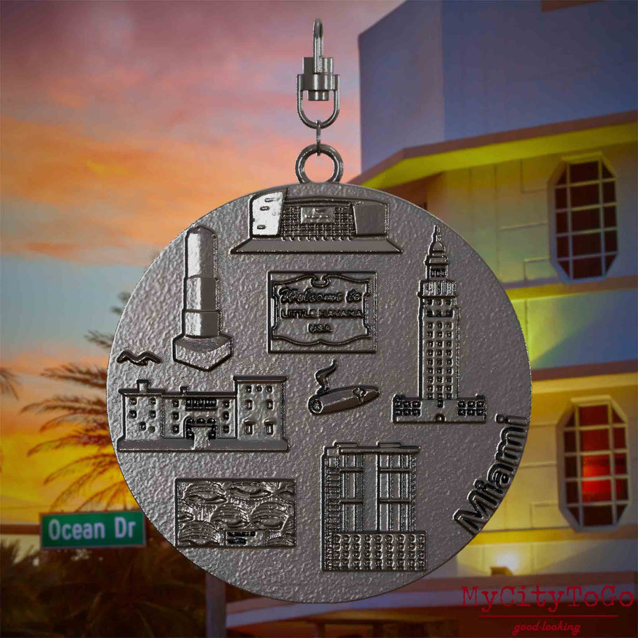 Halskette mit Drehwirbel und Vorderseite eines Schmuckanhängers aus Titan, auf dem Reliefs bekannter Sehenswürdigkeiten der Stadt Miami abgebildet sind. Den Hintergrund bildet eine Ansicht der Stadt Miami.
