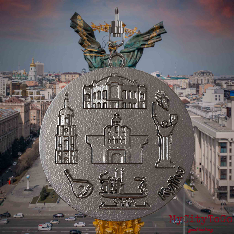 Halskette mit Drehwirbel und Vorderseite eines Schmuckanhängers aus Titan, auf dem Reliefs bekannter Sehenswürdigkeiten der Stadt Kyjiw abgebildet sind. Den Hintergrund bildet eine Ansicht der Stadt Kyjiw.



