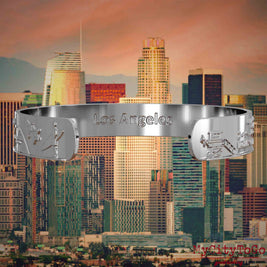 Innenseite eines silbernen Armreifs mit Reliefs bekannter Sehenswürdigkeiten der Stadt Los Angeles und einer Gravur des Stadtnamens. Den Hintergrund bildet eine Ansicht der Stadt Los Angeles.