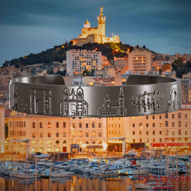 Armreif aus Titan mit Reliefs bekannter Sehenswürdigkeiten der Stadt Marseille. Den Hintergrund bildet eine Ansicht der Stadt Marseille.