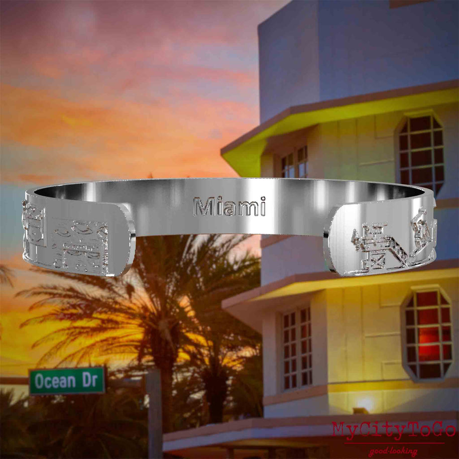 Innenseite eines silbernen Armreifs mit Reliefs bekannter Sehenswürdigkeiten der Stadt Miami und einer Gravur des Stadtnamens. Den Hintergrund bildet eine Ansicht der Stadt Miami.