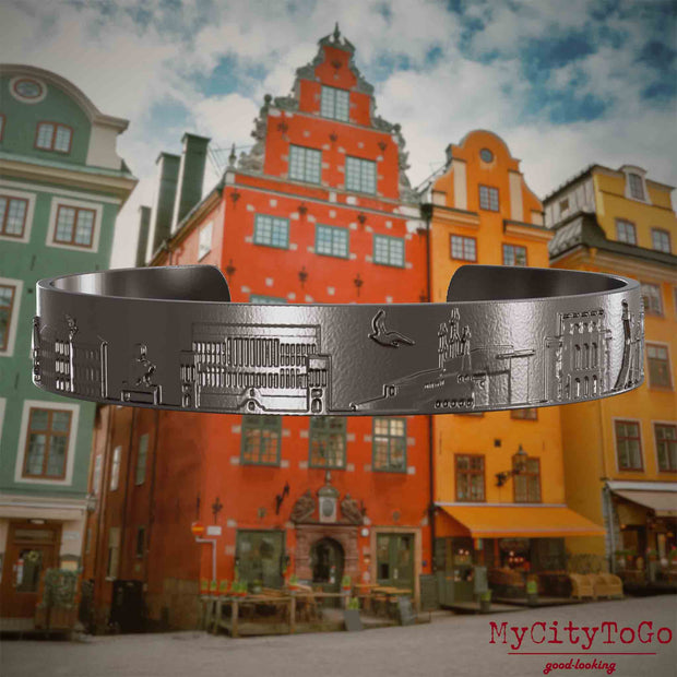 Armreif aus Titan mit Reliefs bekannter Sehenswürdigkeiten der Stadt Stockholm. Den Hintergrund bildet eine Ansicht der Stadt Stockholm.