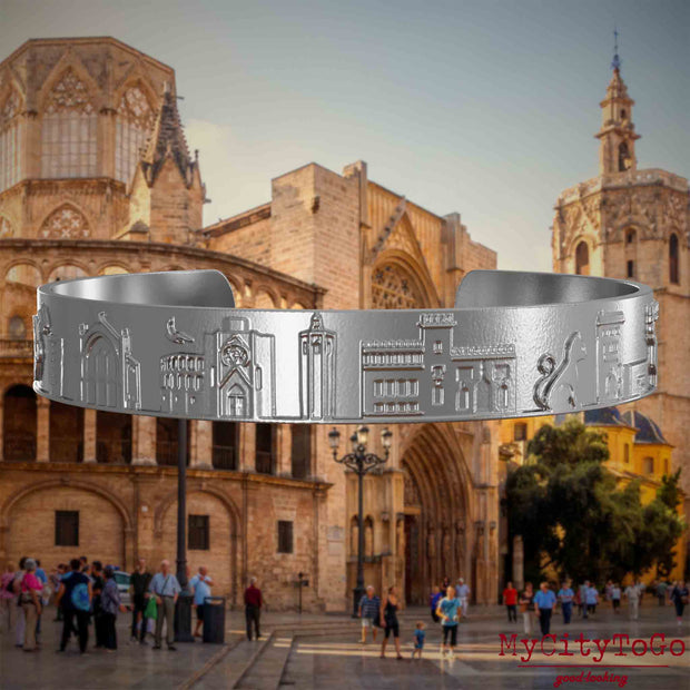 Armreif aus Edelstahl mit Reliefs bekannter Sehenswürdigkeiten der Stadt Valencia. Den Hintergrund bildet eine Ansicht der Stadt Valencia.