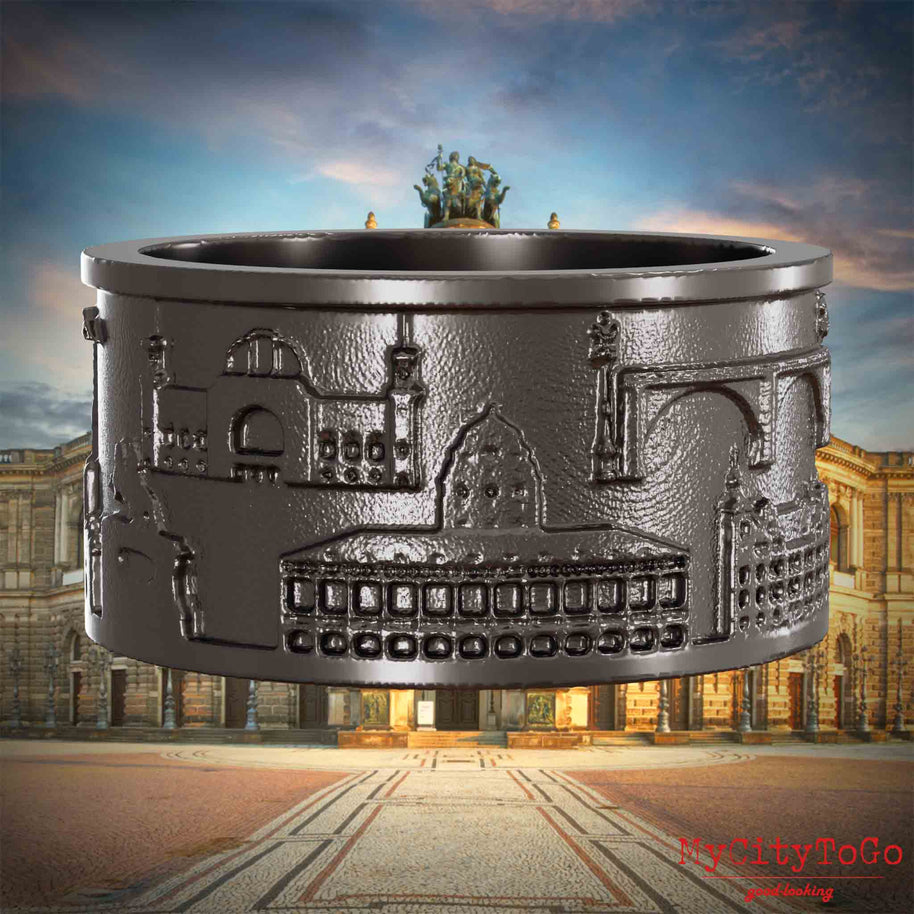 Ring aus Titan mit Reliefs bekannter Sehenswürdigkeiten der Stadt Dresden. Den Hintergrund bildet eine Ansicht der Stadt Dresden.