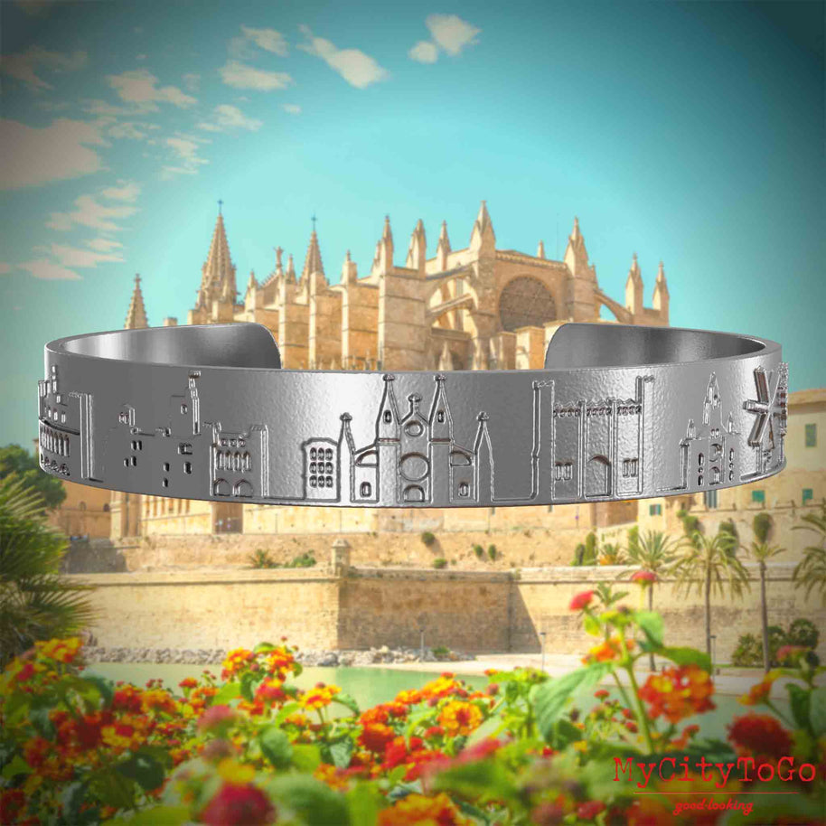 Armreif aus Edelstahl mit Reliefs bekannter Sehenswürdigkeiten der Stadt Palma de Mallorca. Den Hintergrund bildet eine Ansicht der Stadt Palma de Mallorca.