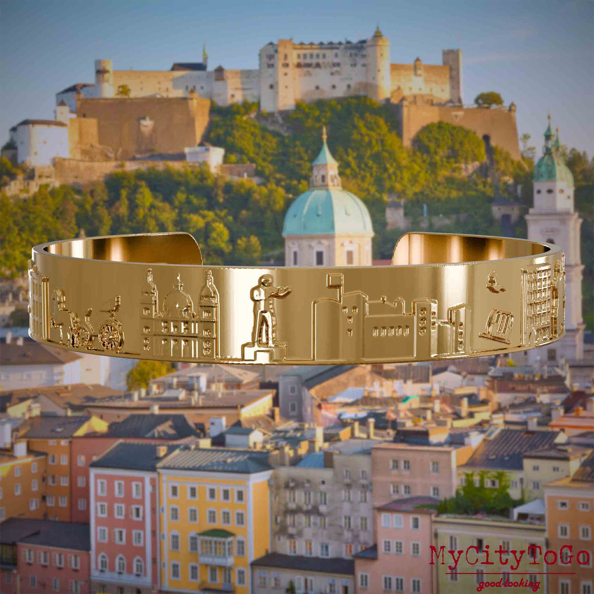 Vergoldeter Armreif mit Reliefs bekannter Sehenswürdigkeiten der Stadt Salzburg. Den Hintergrund bildet eine Ansicht der Stadt Salzburg.