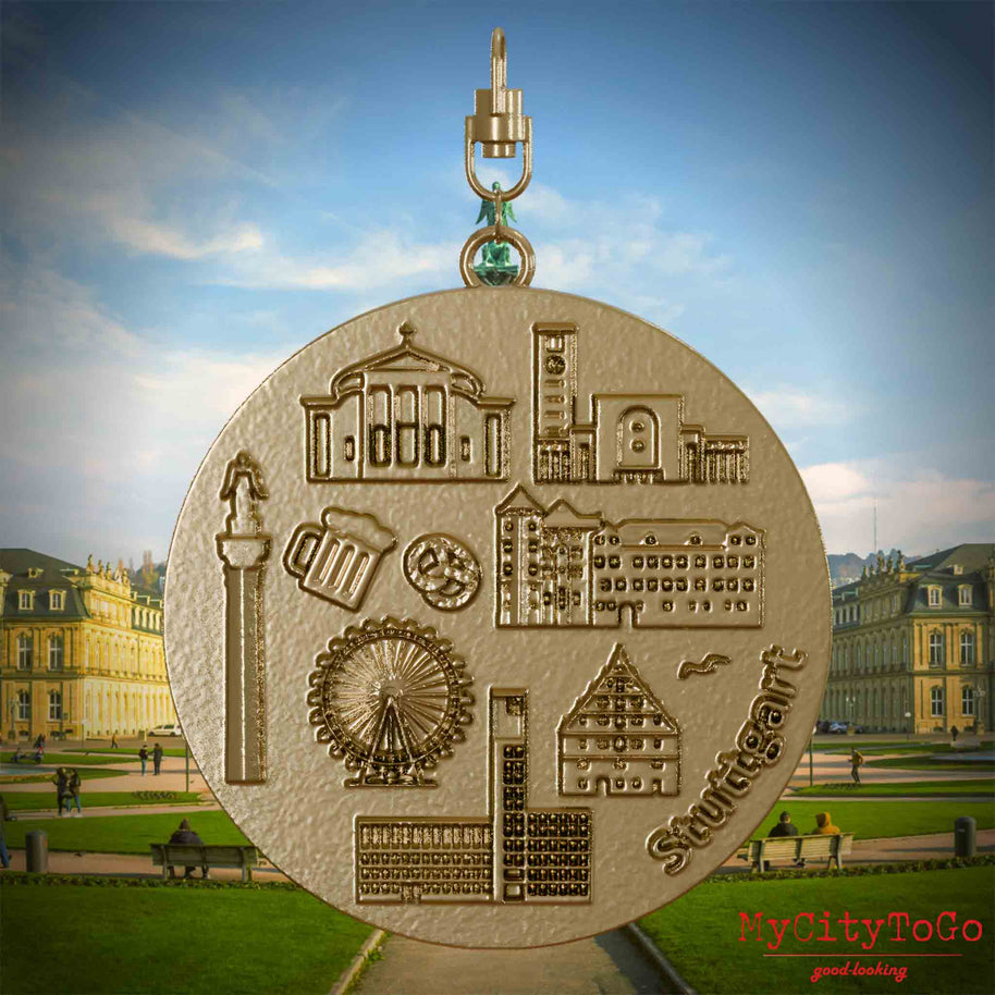 Halskette mit Drehwirbel und Rückseite eines Schmuckanhängers aus vergoldetem Edelstahl, auf dem Reliefs bekannter Sehenswürdigkeiten der Stadt Stuttgart abgebildet sind. Den Hintergrund bildet eine Ansicht der Stadt Stuttgart.
