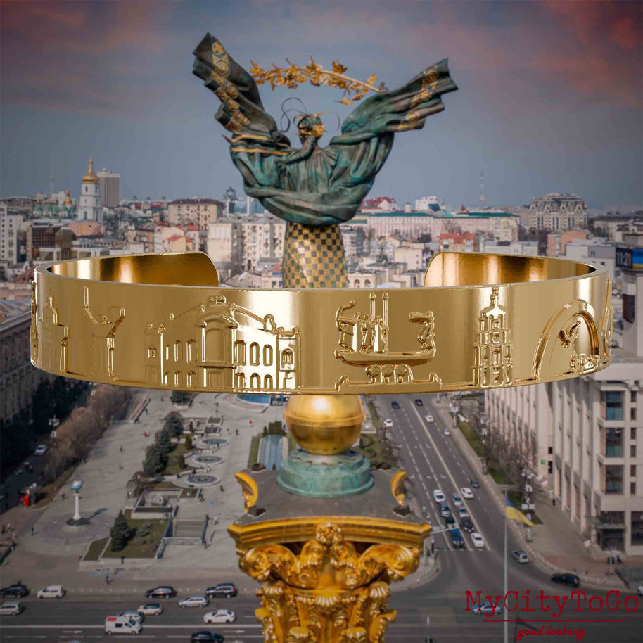Vergoldeter Armreif mit Reliefs bekannter Sehenswürdigkeiten der Stadt Kiew. Den Hintergrund bildet eine Ansicht der Stadt Kiew.
