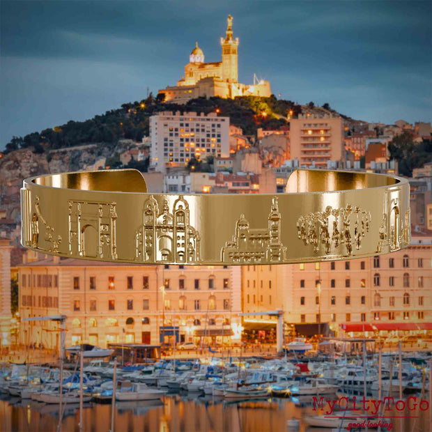Vergoldeter Armreif mit Reliefs bekannter Sehenswürdigkeiten der Stadt Marseille. Den Hintergrund bildet eine Ansicht der Stadt Marseille.