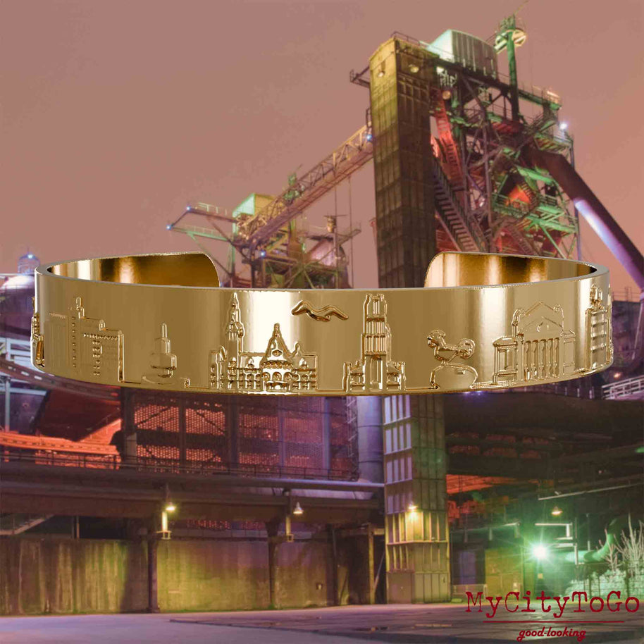 Gold-plated Bangle with reliefs of well-known landmarks of the city of Duisburg. The background features a view of the city of Duisburg.