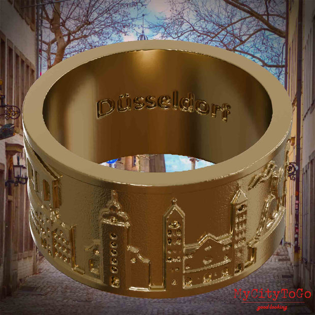 Ring aus vergoldetem Edelstahl mit Reliefs bekannter Sehenswürdigkeiten der Stadt Duesseldorf und einer Gravur des Stadtnamens auf der Innenseite. Den Hintergrund bildet eine Ansicht der Stadt Duesseldorf.