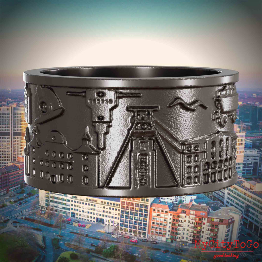 Ring aus Titan mit Reliefs bekannter Sehenswürdigkeiten der Stadt Essen. Den Hintergrund bildet eine Ansicht der Stadt Essen.