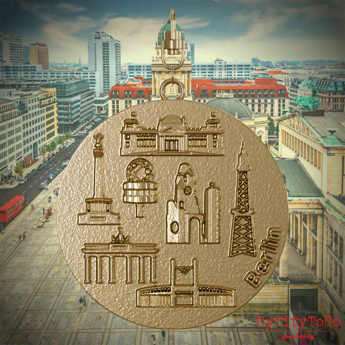 Halskette mit Drehwirbel und Rückseite eines Schmuckanhängers aus vergoldetem Edelstahl, auf dem Reliefs bekannter Sehenswürdigkeiten der Stadt Berlin abgebildet sind. Den Hintergrund bildet eine Ansicht der Stadt Berlin.
