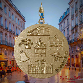 Halskette mit Drehwirbel und Rückseite eines Schmuckanhängers aus vergoldetem Edelstahl, auf dem Reliefs bekannter Sehenswürdigkeiten der Stadt Bordeaux abgebildet sind. Den Hintergrund bildet eine Ansicht der Stadt Bordeaux.
