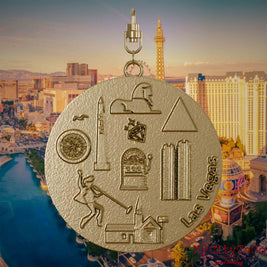 Necklace with swivel clasp and the front of a jewelry pendant made of gold-plated stainless steel, featuring reliefs of well-known Las Vegas landmarks. The background shows a view of the city of Las Vegas.