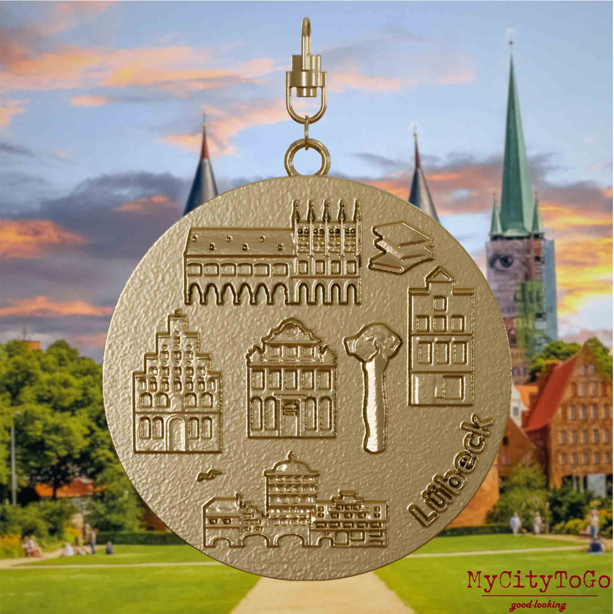 Halskette mit Drehwirbel und Vorderseite eines Schmuckanhängers aus vergoldetem Edelstahl, auf dem Reliefs bekannter Sehenswürdigkeiten der Stadt Luebeck abgebildet sind. Den Hintergrund bildet eine Ansicht der Stadt Luebeck.

