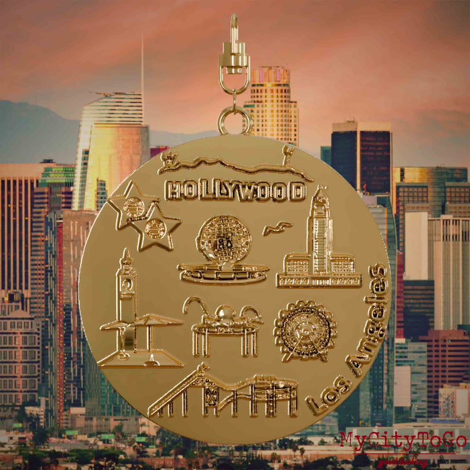 Halskette mit Drehwirbel und Vorderseite eines vergoldeten Schmuckanhängers, auf dem Reliefs bekannter Sehenswürdigkeiten der Stadt Los Angeles abgebildet sind. Den Hintergrund bildet eine Ansicht der Stadt Los Angeles.

