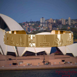Vergoldeter Armreif mit Reliefs bekannter Sehenswürdigkeiten der Stadt Sydney. Den Hintergrund bildet eine Ansicht der Stadt Sydney.