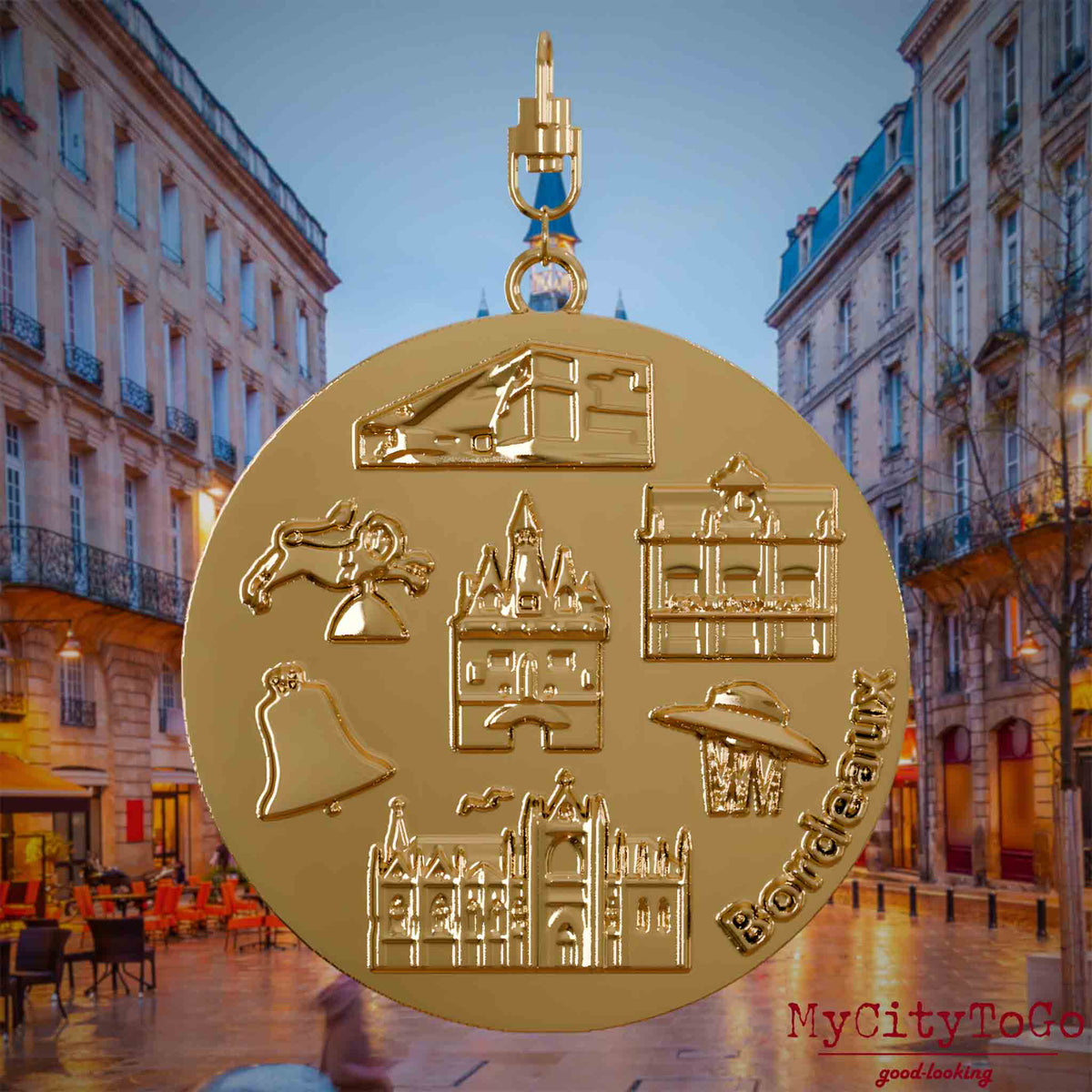 Halskette mit Drehwirbel und Rückseite eines vergoldeten Schmuckanhängers, auf dem Reliefs bekannter Sehenswürdigkeiten der Stadt Bordeaux abgebildet sind. Den Hintergrund bildet eine Ansicht der Stadt Bordeaux.
