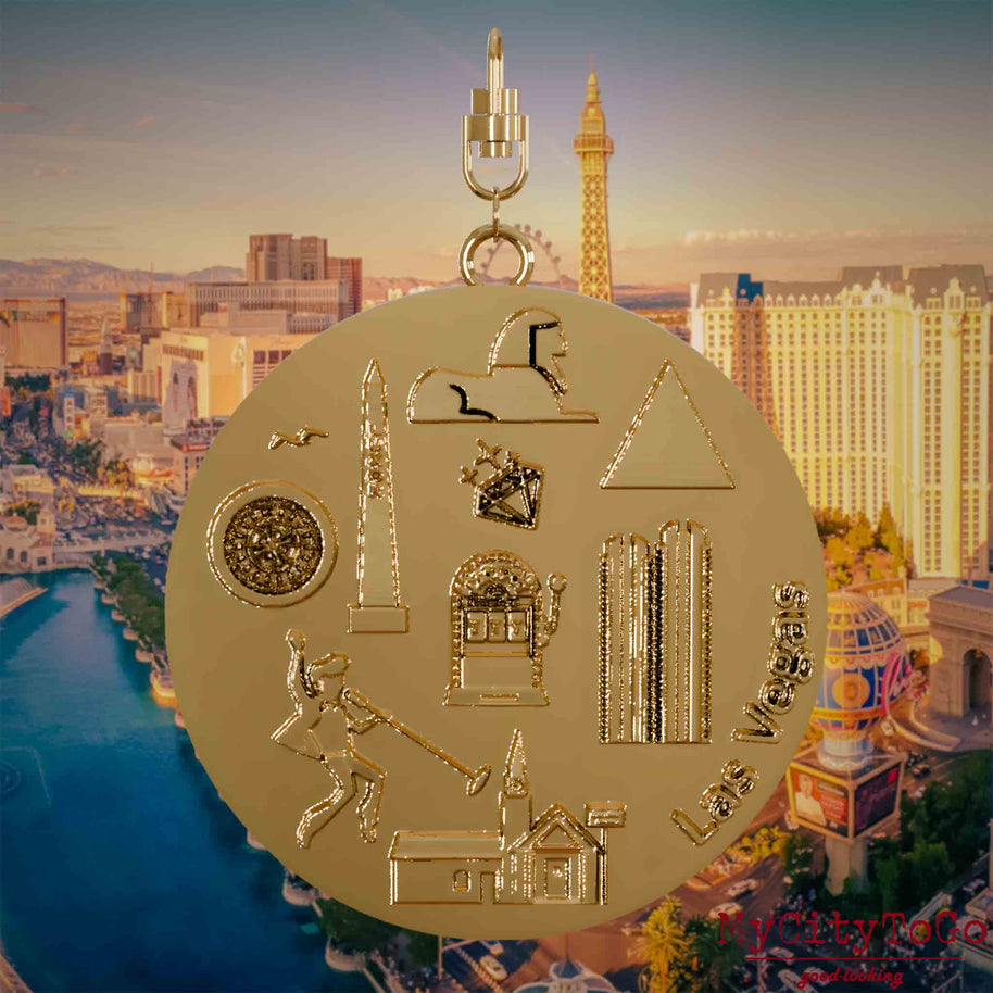 Necklace with a swivel clasp and the front of a gold-plated jewelry pendant featuring reliefs of famous Las Vegas landmarks. The background shows a view of the city of Las Vegas.
