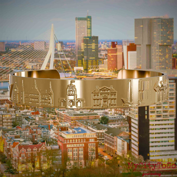 Vergoldeter Armreif mit Reliefs bekannter Sehenswürdigkeiten der Stadt Rotterdam. Den Hintergrund bildet eine Ansicht der Stadt Rotterdam.