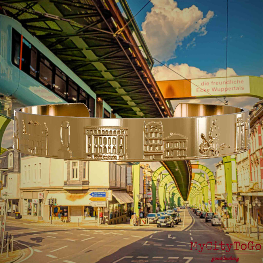 Vergoldeter Armreif mit Reliefs bekannter Sehenswürdigkeiten der Stadt Wuppertal. Den Hintergrund bildet eine Ansicht  der Stadt Wuppertal.